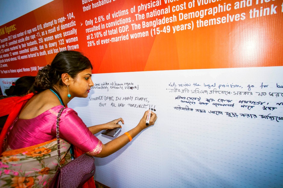A woman writes on a pledge board at Orange the World 2018 in Bangladesh, marking 16 Days of Activism Against Gender-Based Violence
